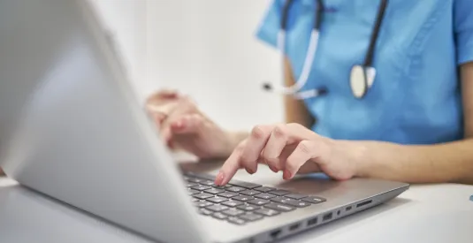 Close-up hands of physician in medical uniform working typing on laptop keyboard sitting at desk