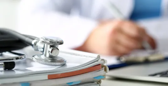 Stethoscope head lying on medical forms on clipboard closeup while medicine doctor working in background.